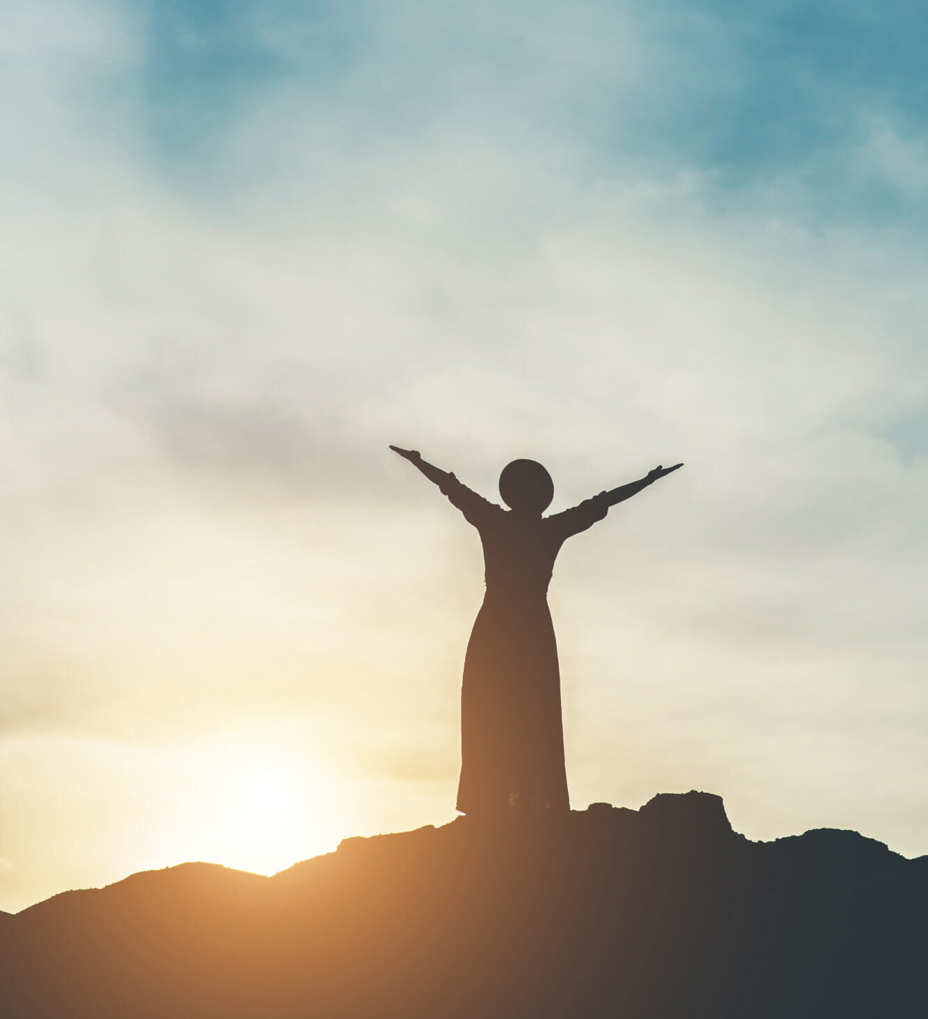 A woman in silhouette stands on a hill facing the rising sun